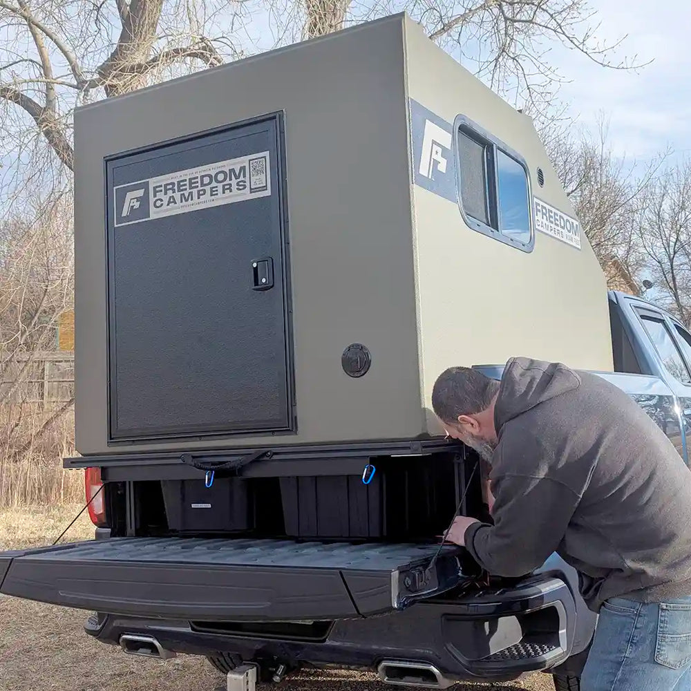 Man attaching a Freedom Campers trailer elevated by PLAT platform to a truckbed in an outdoor setting